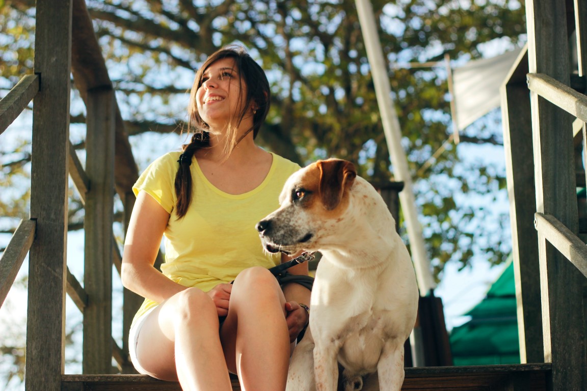 Budgetpetcare Woman sitting on steps with her dog in an outside setting under a tree